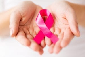 healthcare, charity, people and medicine concept - close up of woman cupped hands holding pink cancer awareness ribbon