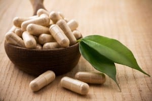 Alternative medicine tablets on a wooden spoon, green leaf.