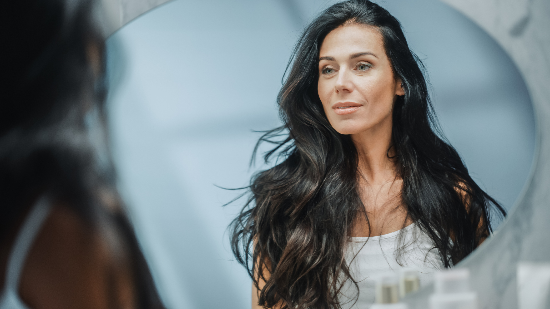 Beautiful Caucasian Middle Aged Woman Looks into Bathroom Mirror, Enjoys Her Looks. Concept for Happiness, Wellbeing, Natural Beauty and Organic Skin Care Products Yearly Skin Check